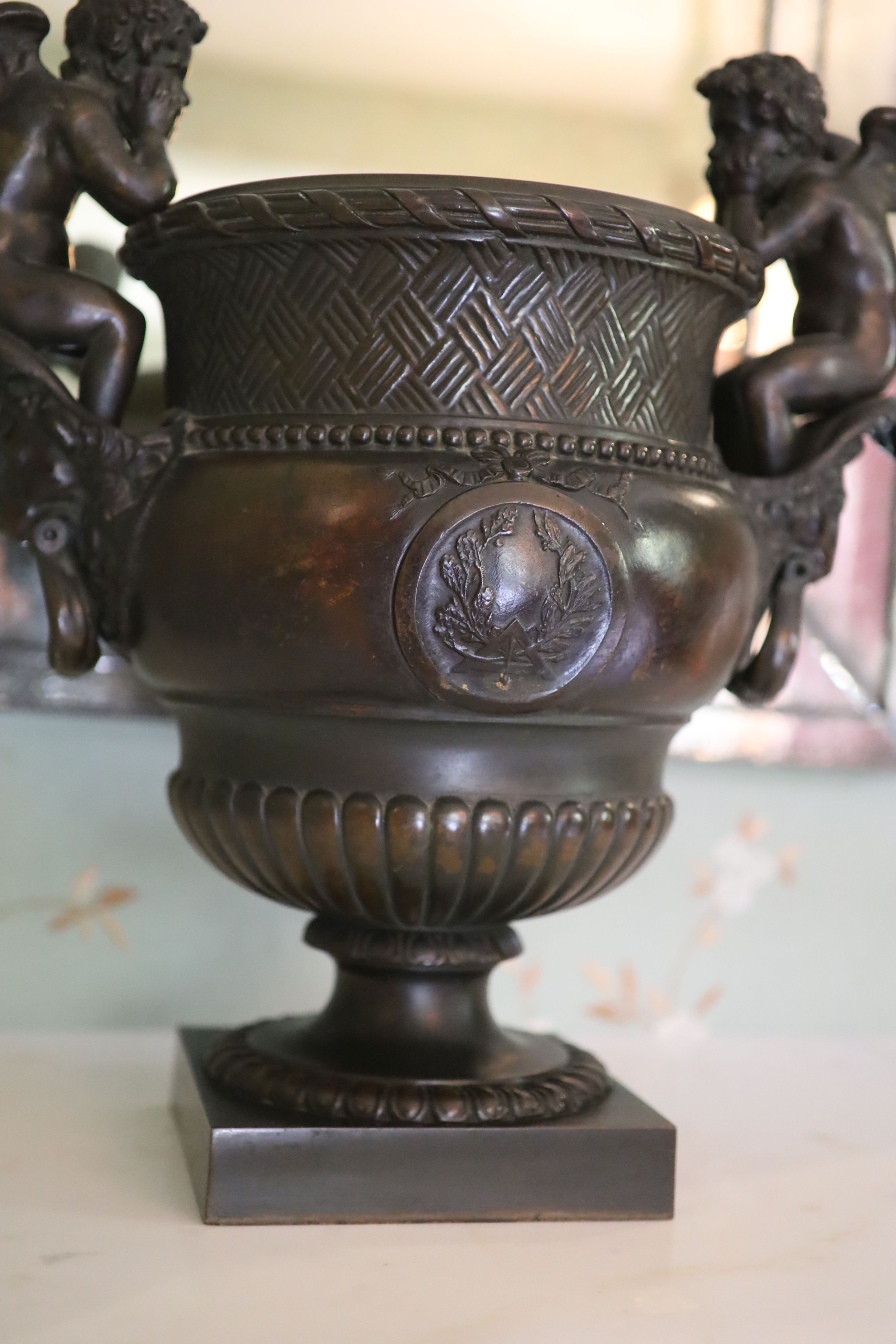 A classical style bronze urn modelled with disconsulate cherubs, height 44cm width 40cm